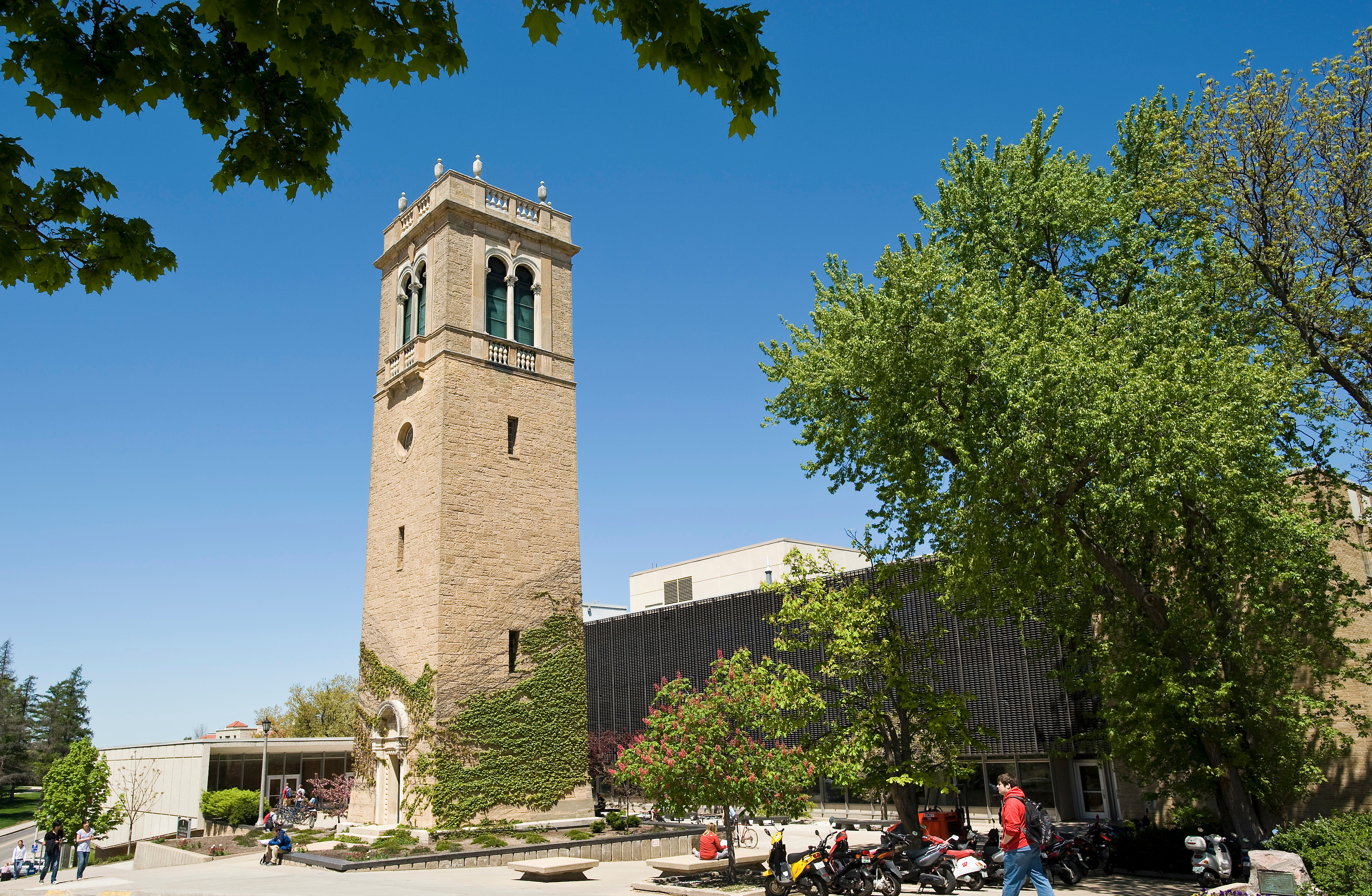 A picture of trees and pedestrians frame a view of the Carillon Tower in front of the Sewell Social Sciences Building.